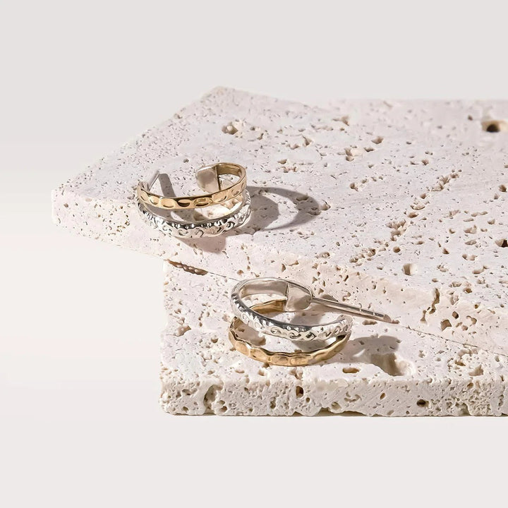 Niche Jewellery Charlotte's Web Aura Magic mixed metal double hoop earrings with silver and bronze floral motifs on stone display.