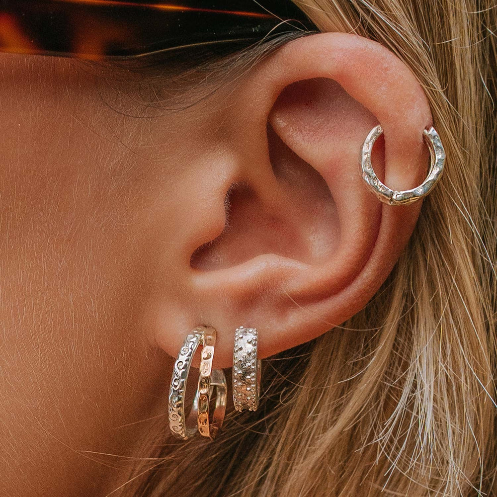 Niche Jewellery Charlotte's Web Aura Magic mixed metal hoop earrings with silver and bronze floral motifs on an ear.