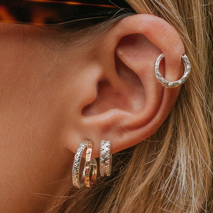 Niche Jewellery Charlotte's Web Aura Magic mixed metal hoop earrings with silver and bronze floral motifs on an ear.