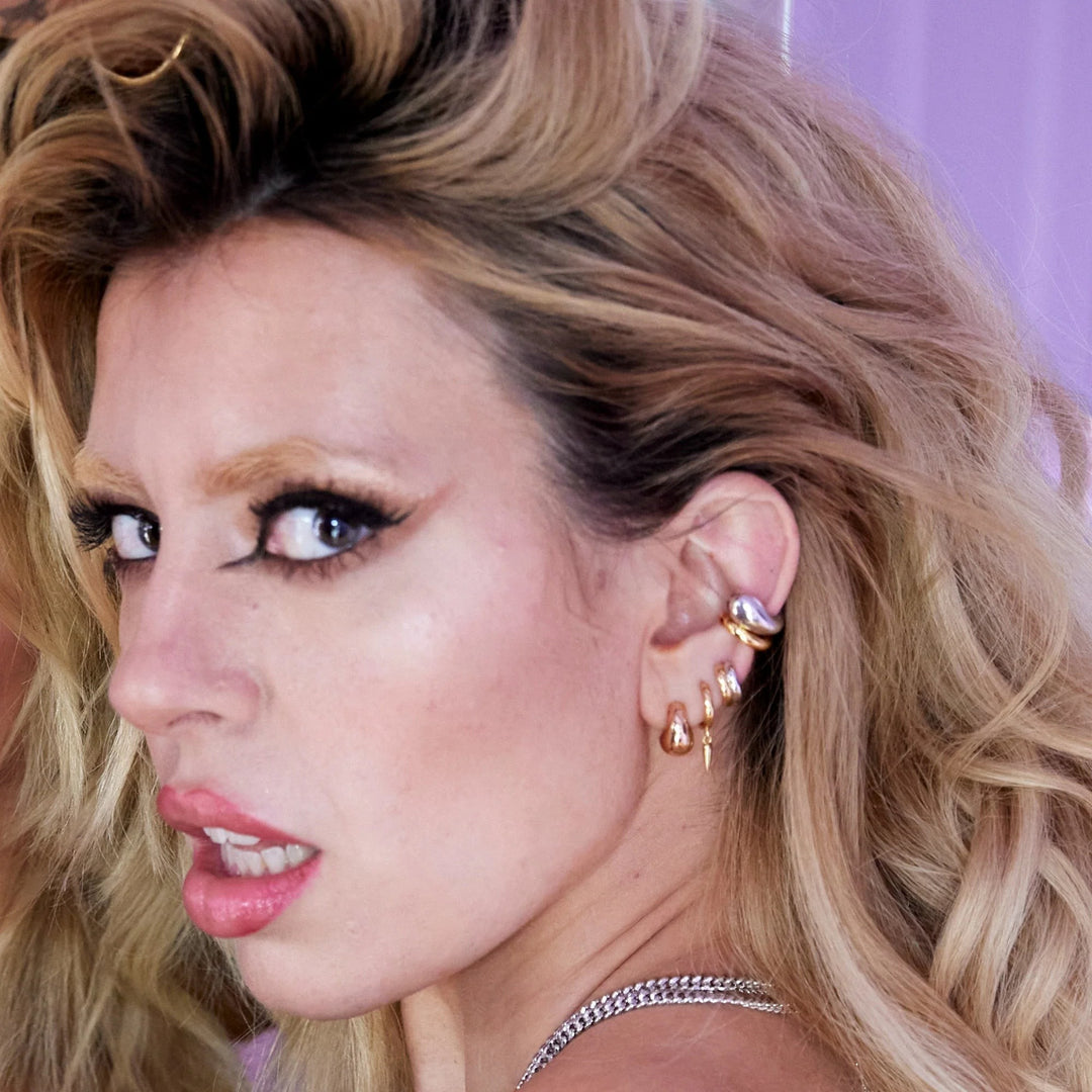 Niche Jewellery Scream Pretty mixed metal huggie earrings worn by a woman with blonde hair against a purple background.