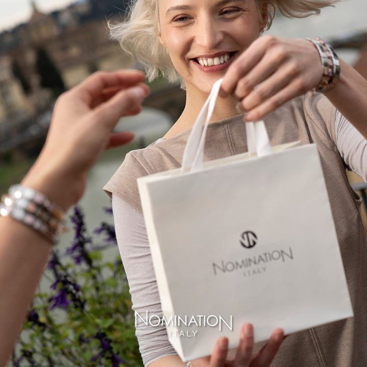Niche Jewellery Nomination branded white paper gift bag held by a smiling woman wearing a charm bracelet