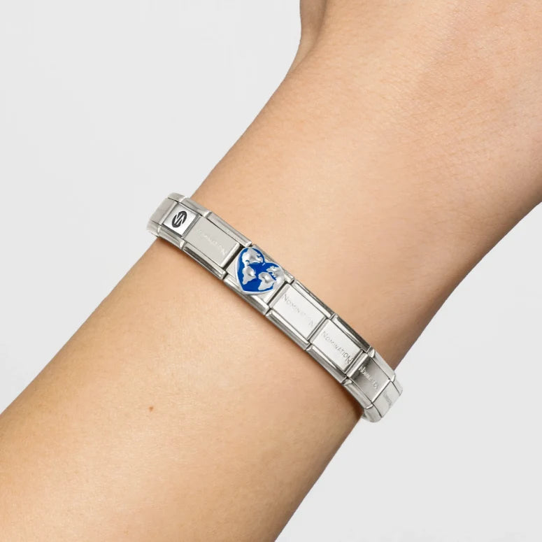 Niche Jewellery Nomination silver heart globe charm with blue enamel on a stainless steel link bracelet on a wrist.