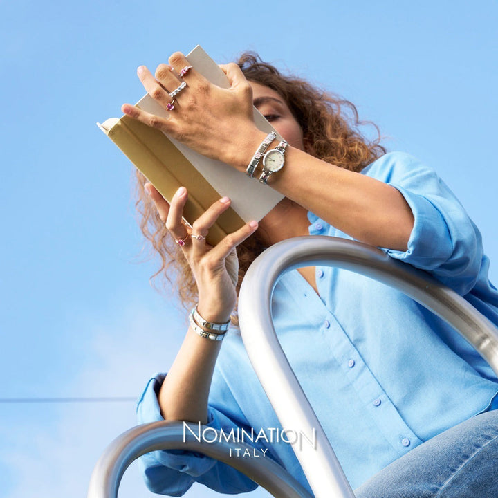 Niche Jewellery Nomination Spain flag charm on a silver composable bracelet worn by a woman reading a book outdoors