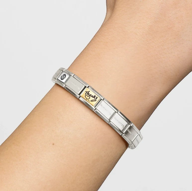 Niche Jewellery Nomination gold and enamel Thanks charm on a stainless steel link bracelet worn on a wrist.