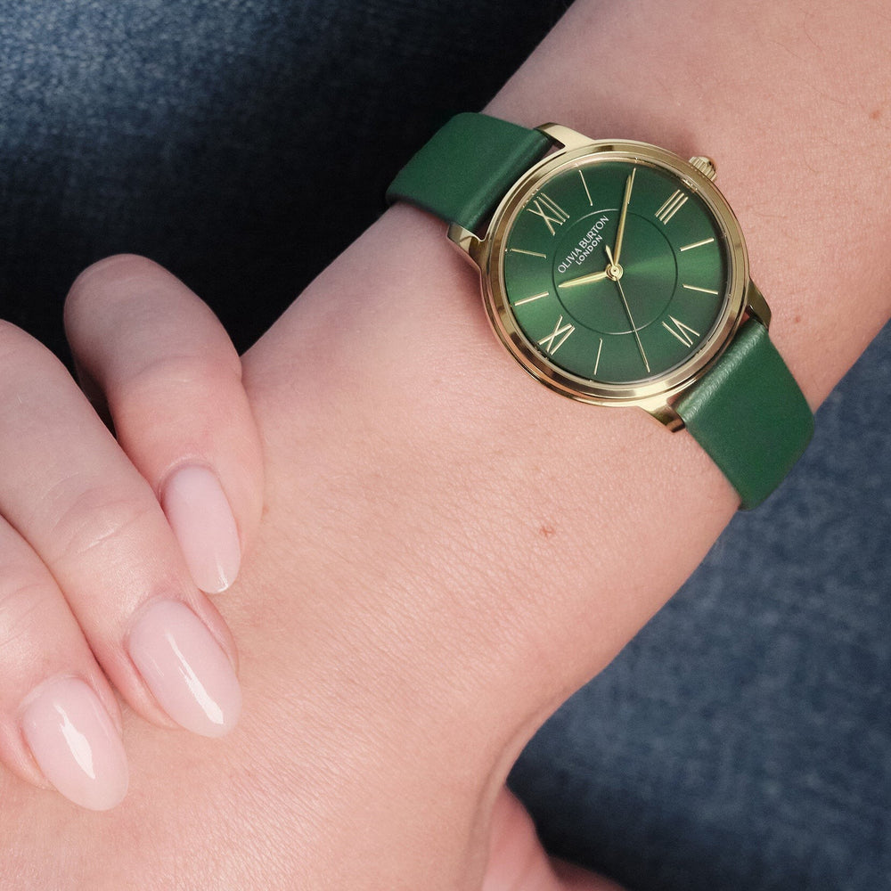 Niche Jewellery Olivia Burton Westbourne watch featuring a gold-tone case and deep green leather strap on a wrist.