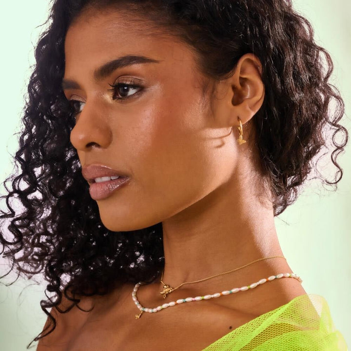Niche Jewellery Annie Haak Papillon gold hoop earrings with butterfly charms worn by a woman with curly hair