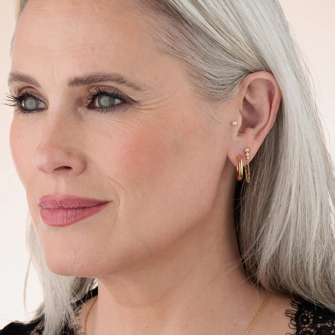 Niche Jewellery Scream Pretty pearl stud earring worn on a model with gold hoop earrings and a delicate chain
