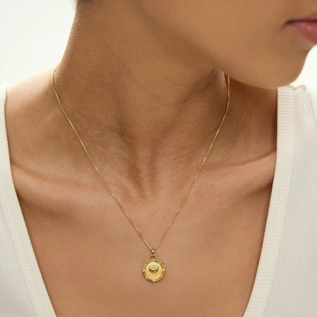 Niche Jewellery Rachel Jackson gold Carpe Diem necklace featuring a circular pendant with heart and wing engravings.