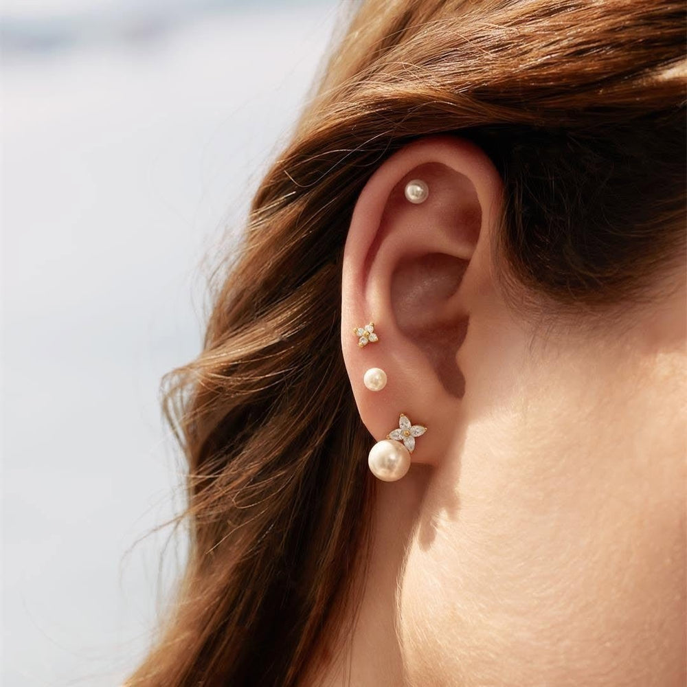 Niche Jewellery Ania Haie silver stud earrings featuring shell pearls and lucky clover charms worn in a layered ear stack