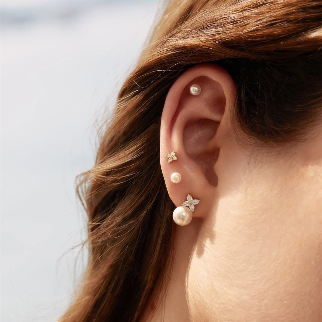 Niche Jewellery Ania Haie silver stud earrings featuring shell pearls and lucky clover charms worn in a layered ear stack