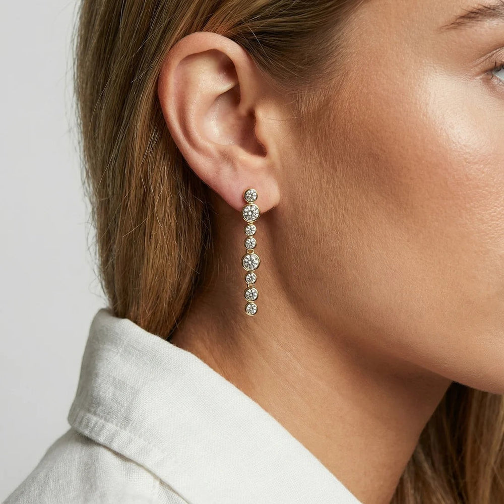 Niche Jewellery Sif Jakobs gold-plated drop earrings featuring a line of sparkling white zirconia stones on a model.