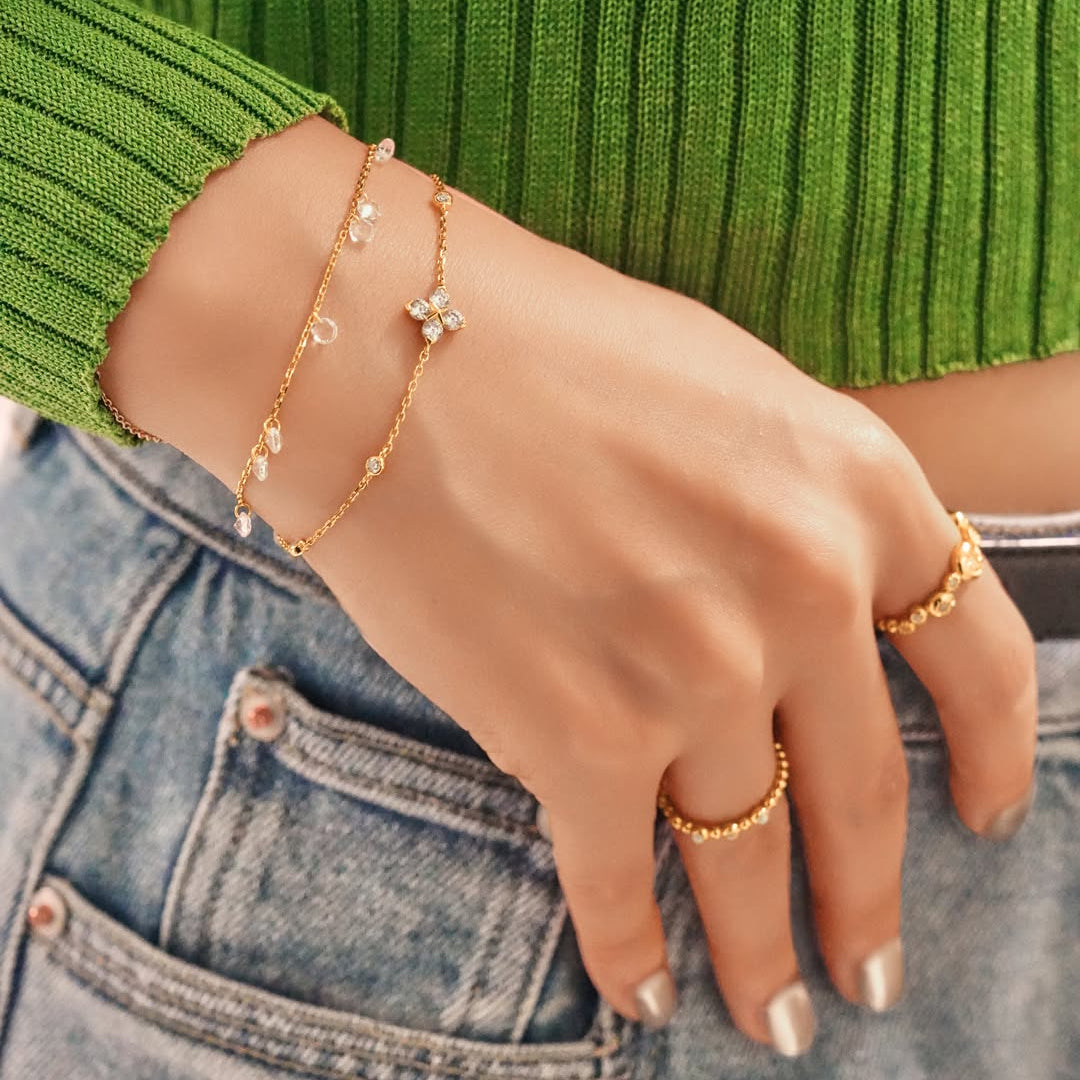 Niche Jewellery Ania Haie gold-tone clover bracelet with sparkling crystals worn on a wrist with stacked rings