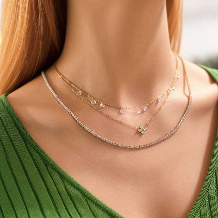Niche Jewellery Ania Haie silver clover necklace layered with delicate gold chains on a woman wearing a green top.