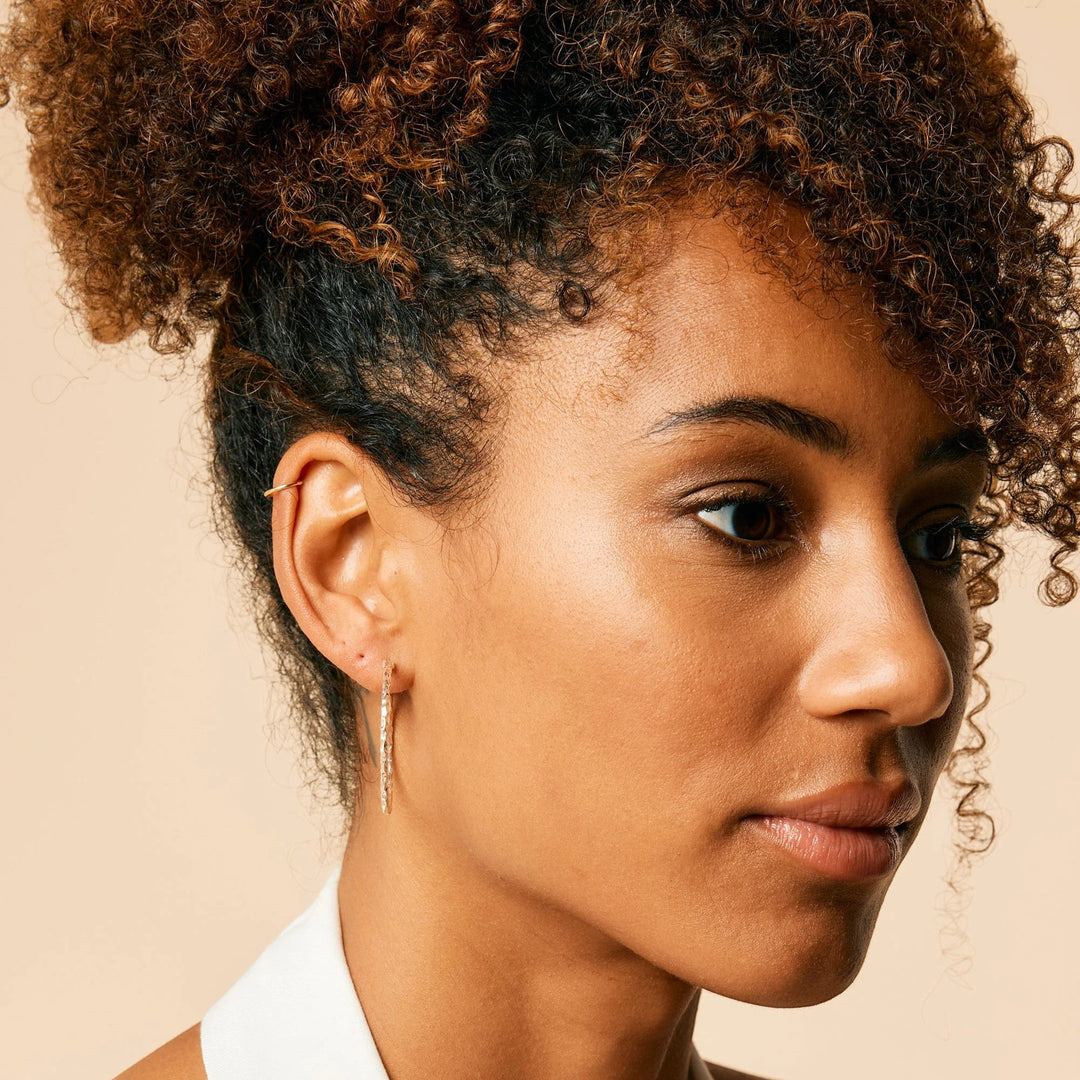 Niche Jewellery Charlotte's Web Jodhpur silver hammered hoop earrings worn by a woman with curly hair