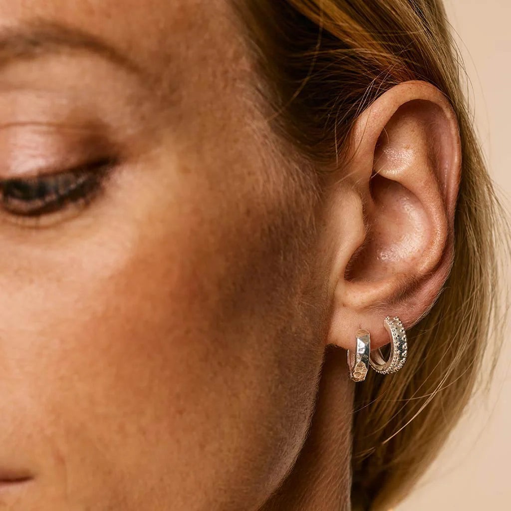 Niche Jewellery Charlotte's Web silver hammered huggie hoops worn on a model's earlobe