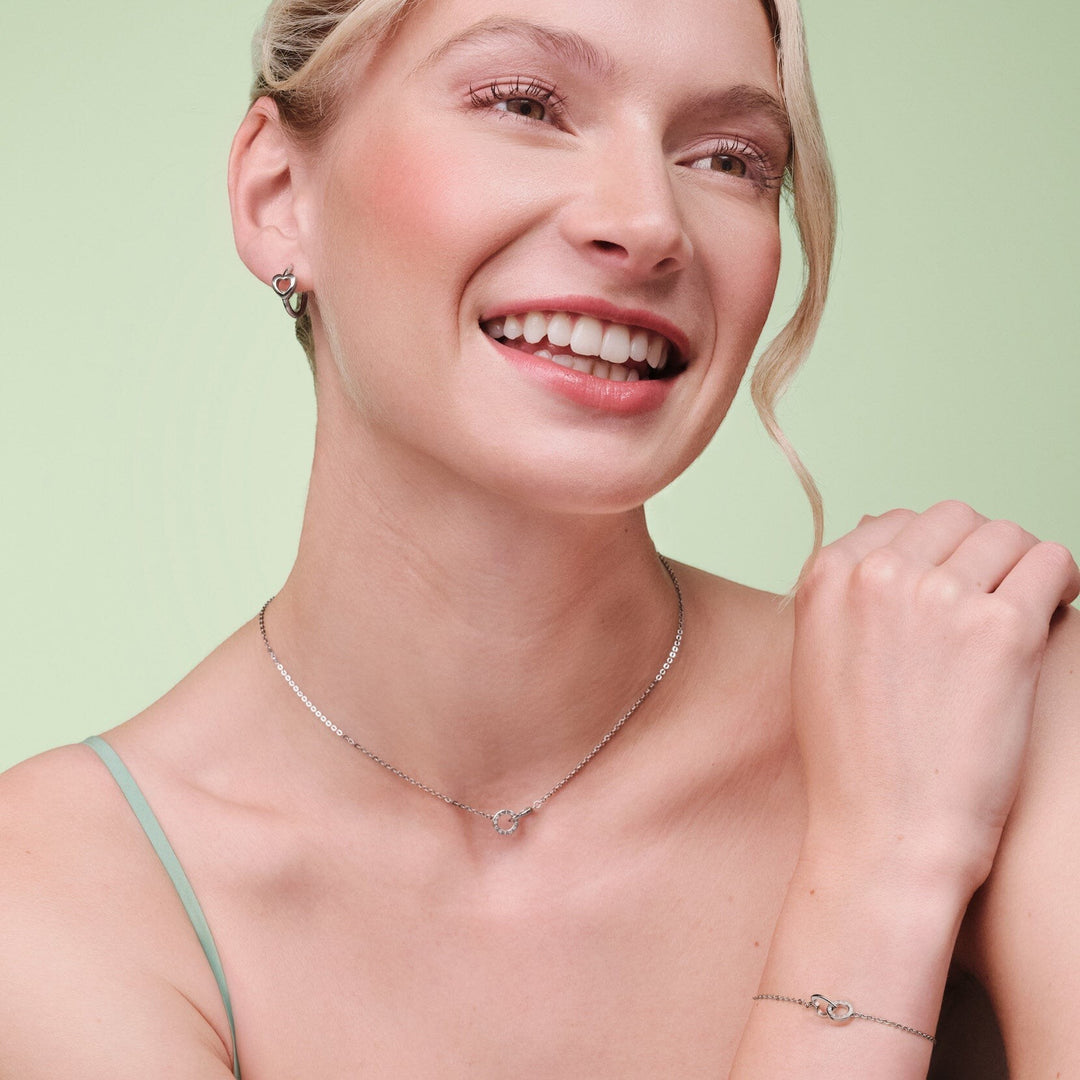 Niche Jewellery Olivia Burton silver-tone hoop earrings with interlinked heart design worn by a smiling woman