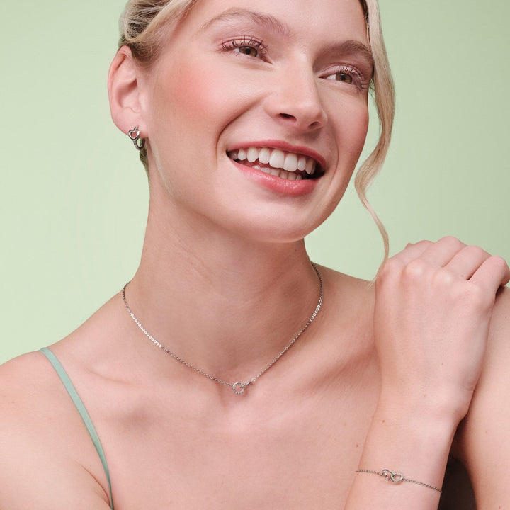 Niche Jewellery Olivia Burton silver-tone hoop earrings with interlinked heart design worn by a smiling woman
