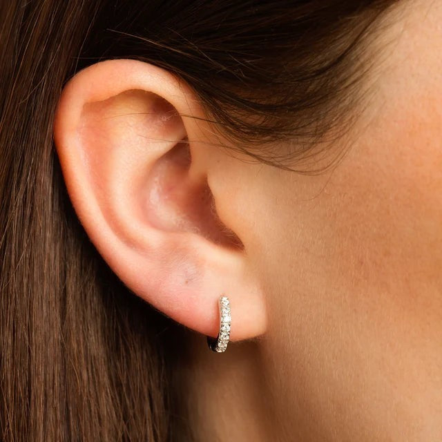 Niche Jewellery Scream Pretty silver huggie hoop earrings featuring a row of clear sparkling stones worn on an ear