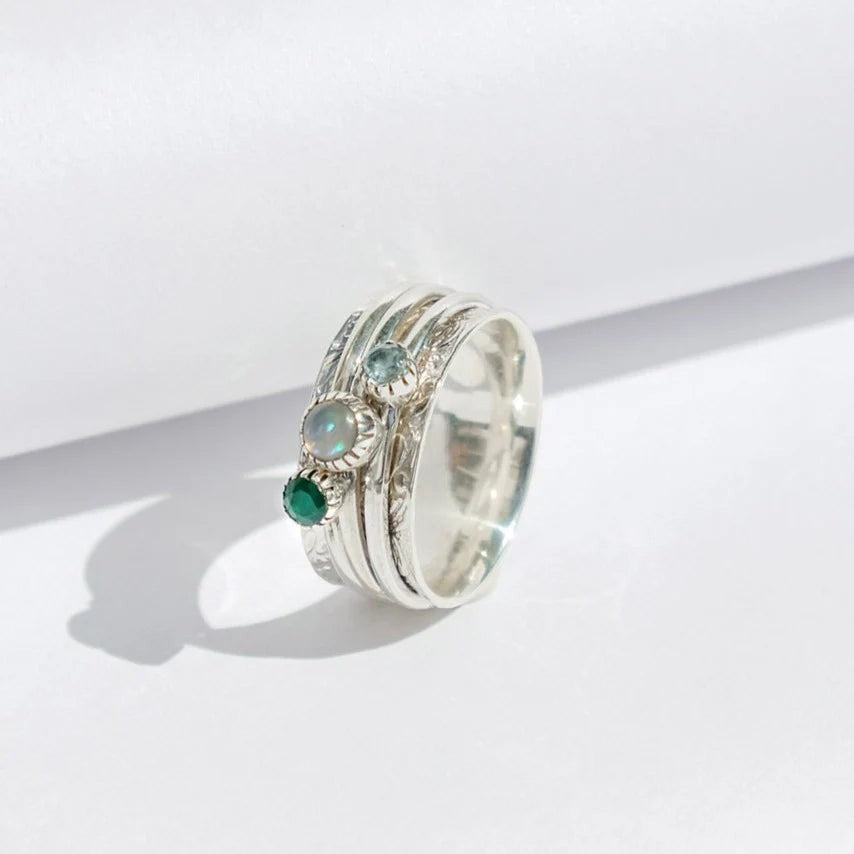 Niche Jewellery Charlotte's Web sterling silver spinning ring with green onyx, opal, and blue topaz stones on a white background.