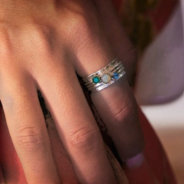 Niche Jewellery Charlotte's Web sterling silver spinning ring with green onyx, opal, and blue topaz stones worn on a finger.
