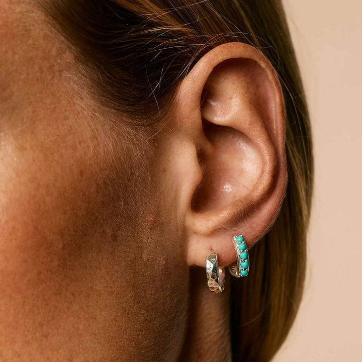 Niche Jewellery Charlotte's Web Kali silver huggie hoops featuring turquoise stones worn on a model's ear.