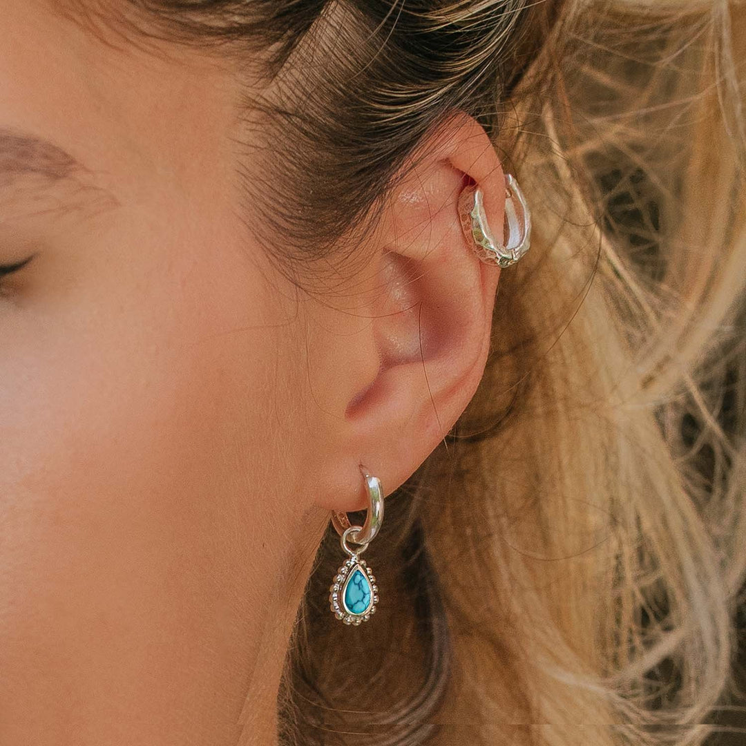 Niche Jewellery Charlotte's Web silver huggie hoop earrings featuring a pear-cut turquoise stone worn on a model's ear