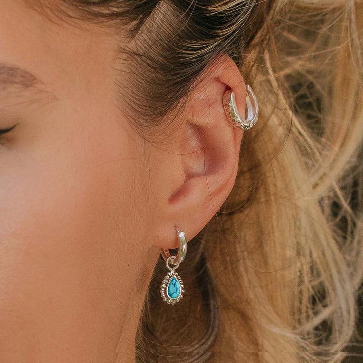 Niche Jewellery Charlotte's Web silver huggie hoop earrings featuring a pear-cut turquoise stone worn on a model's ear