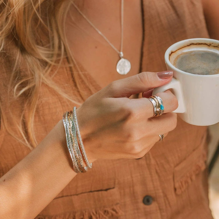 Niche Jewellery Charlotte's Web Aura Magic spinning bangle in sterling silver and brass worn on a woman's wrist.