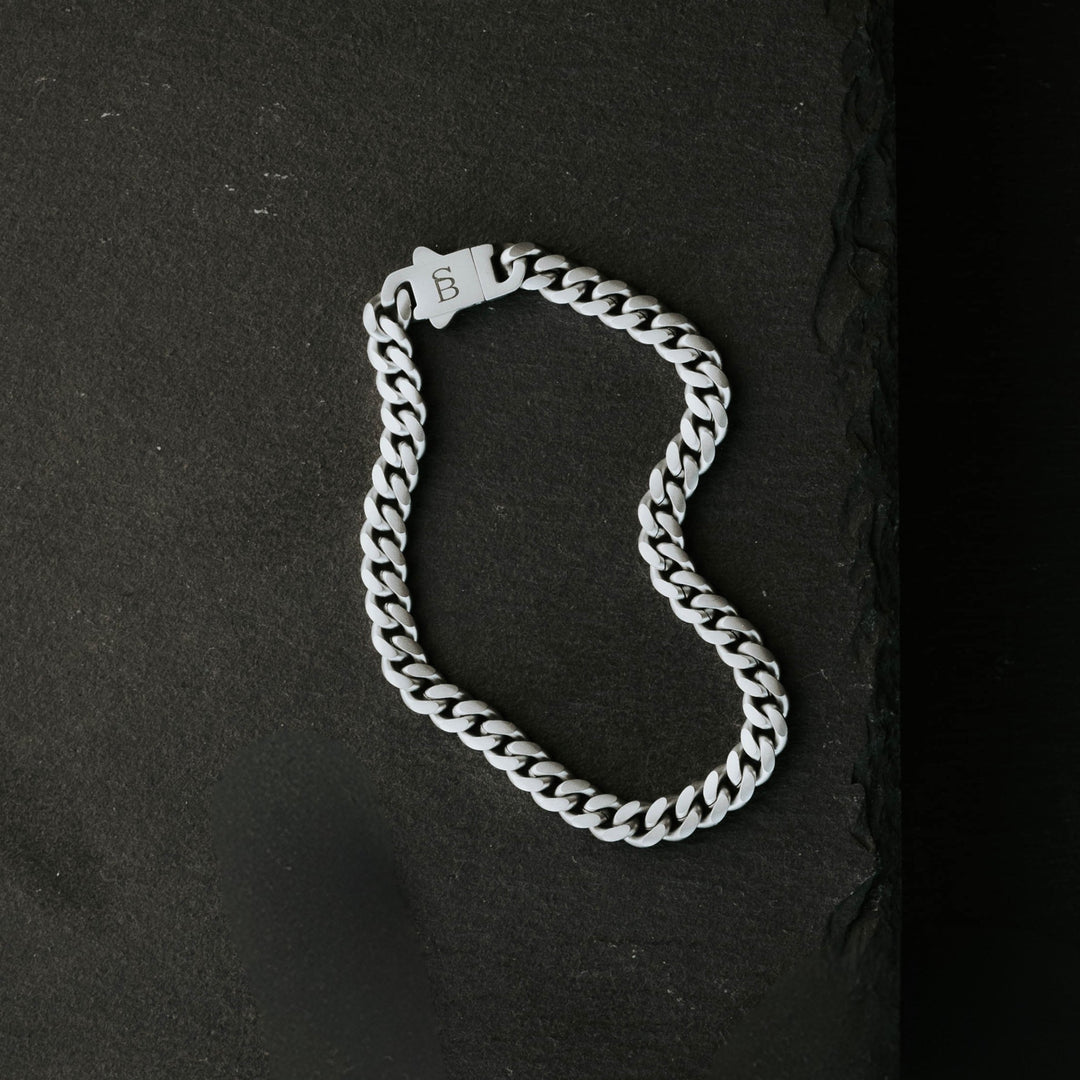Niche Jewellery Steel & Barnett stainless steel link chain bracelet with a branded clasp on a black slate background.