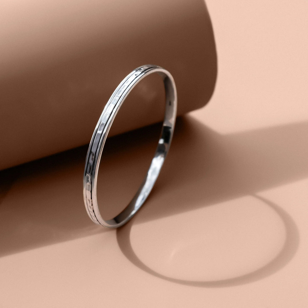 Niche Jewellery Charlotte's Web sterling silver Karma Abundance spinning stacking bangle with a hammered finish on a beige background.