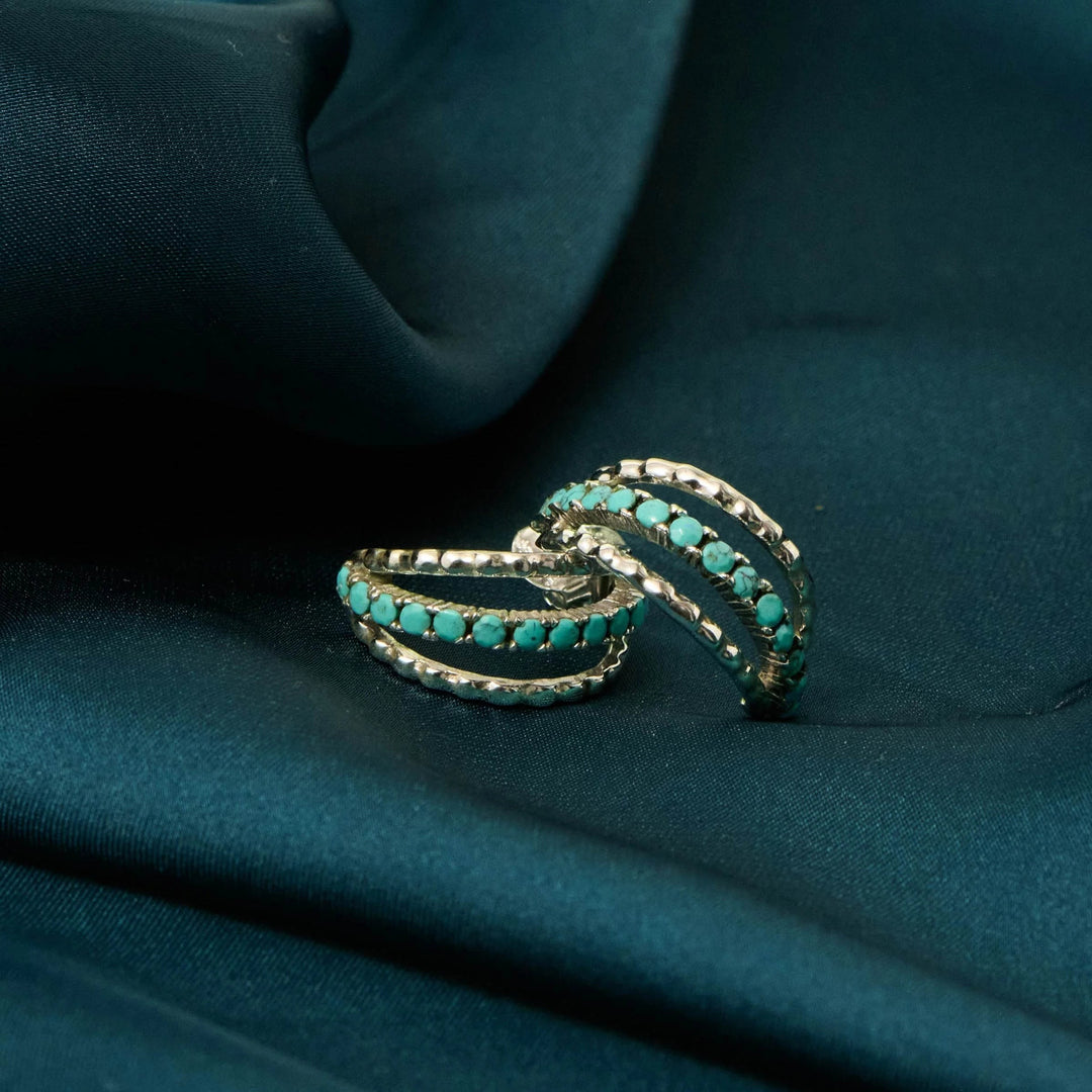 Niche Jewellery Charlotte's Web sterling silver hoop earrings featuring inlaid turquoise stones on a dark teal satin background.