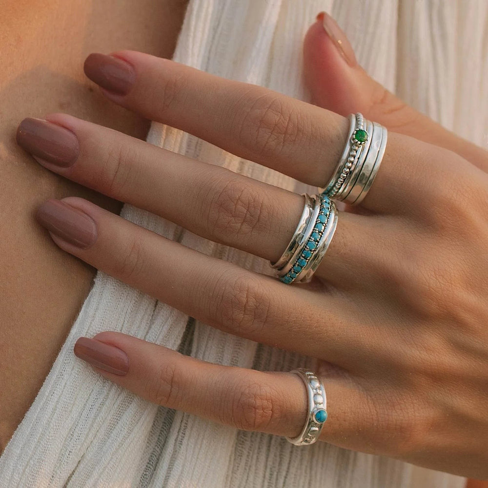 Niche Jewellery Charlotte's Web sterling silver spinning rings with turquoise and green stone accents worn on a woman's hand