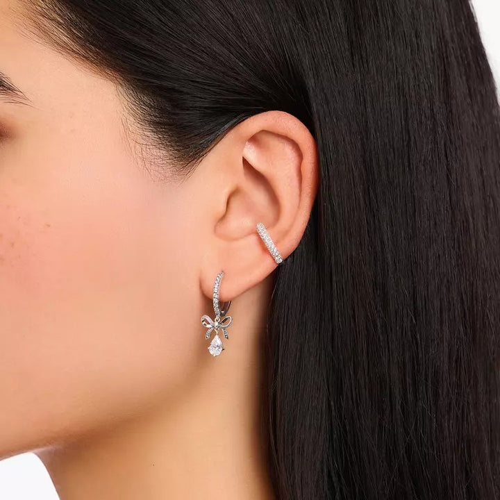Thomas Sabo silver hoop earrings with bow pendant and zirconia stones, set on a model's ear.