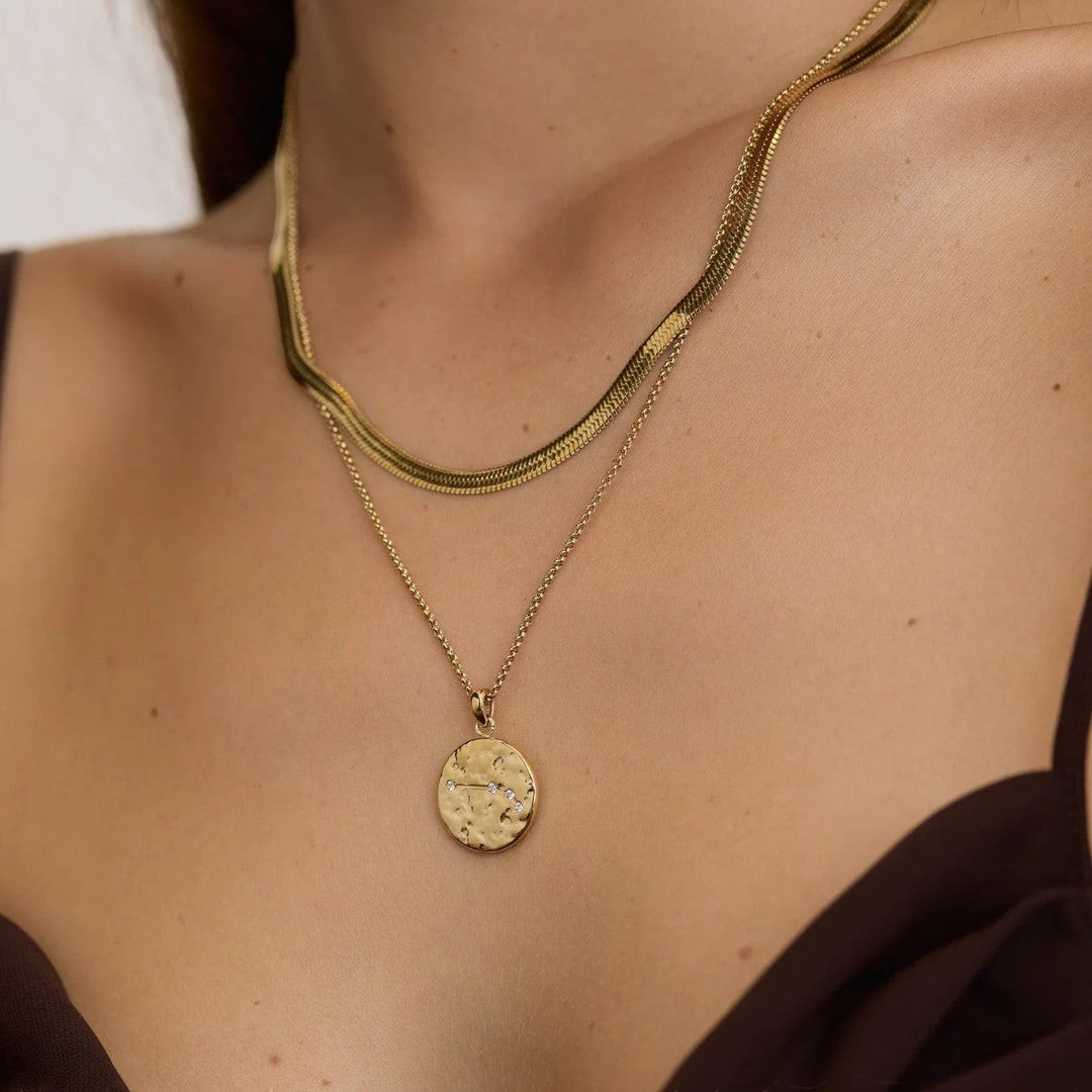DLouise gold Aries zodiac talisman necklace with hammered finish and small crystals, worn layered with a herringbone chain.