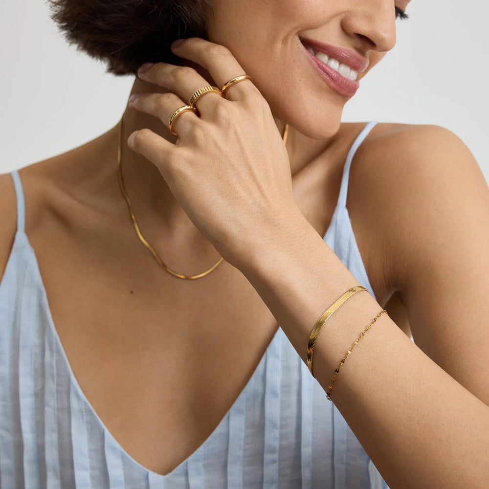Niche Jewellery D. Louise Essentials gold herringbone bracelet and dainty chain bracelet on a woman's wrist.