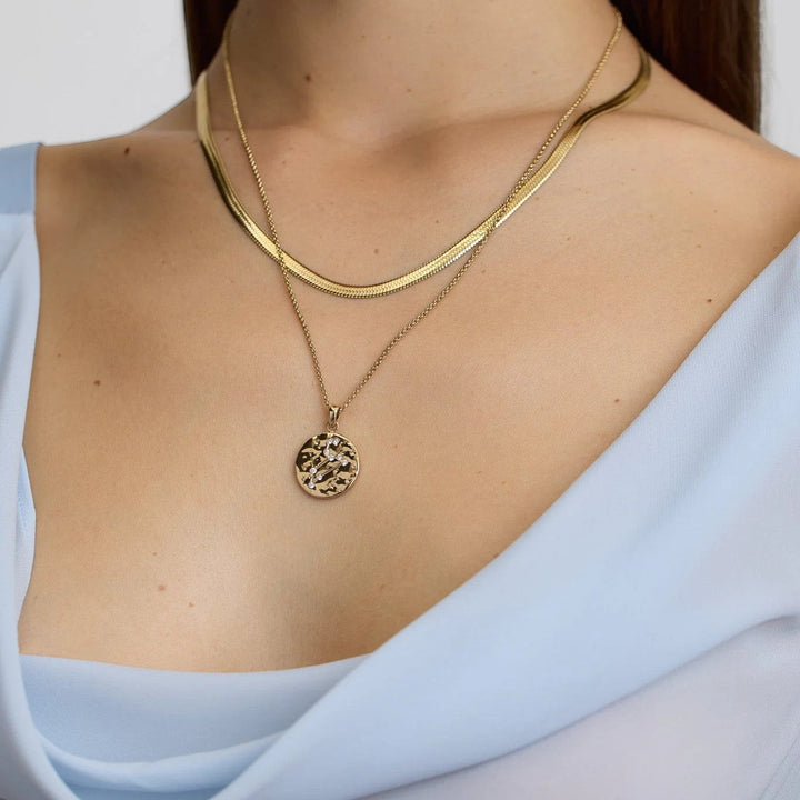 DLouise gold Leo zodiac talisman necklace with hammered finish and crystal accents, layered with a herringbone chain.