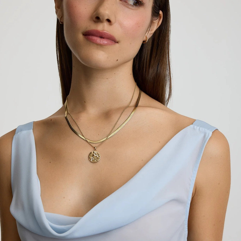 DLouise gold Leo zodiac talisman necklace layered with a herringbone chain on a woman.