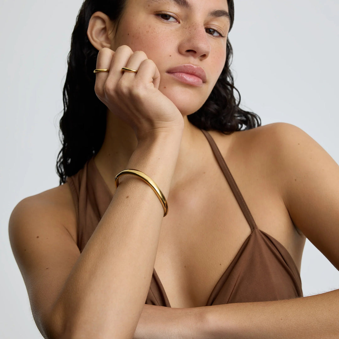 Niche Jewellery gold wave bangle worn by a model, styled with a matching ring. Water and tarnish resistant.