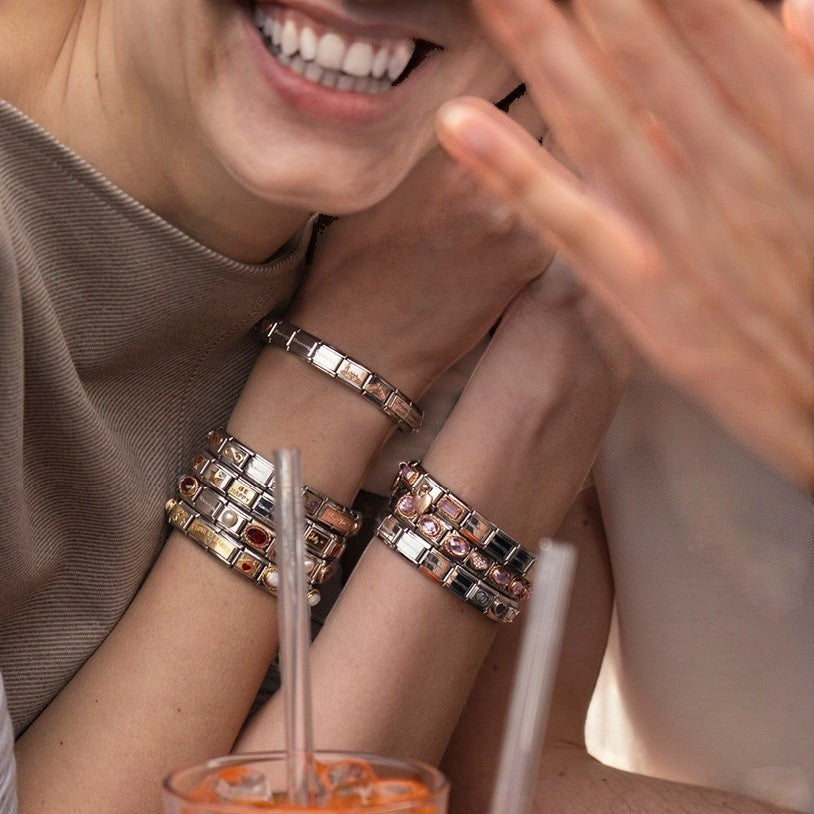 Niche Jewellery Nomination gold and black enamel graduation hat charm on a bracelet worn by a smiling woman.